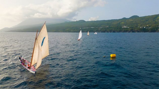 Wideshot of a few whaling boats on the sea with the setting sun and island behind.